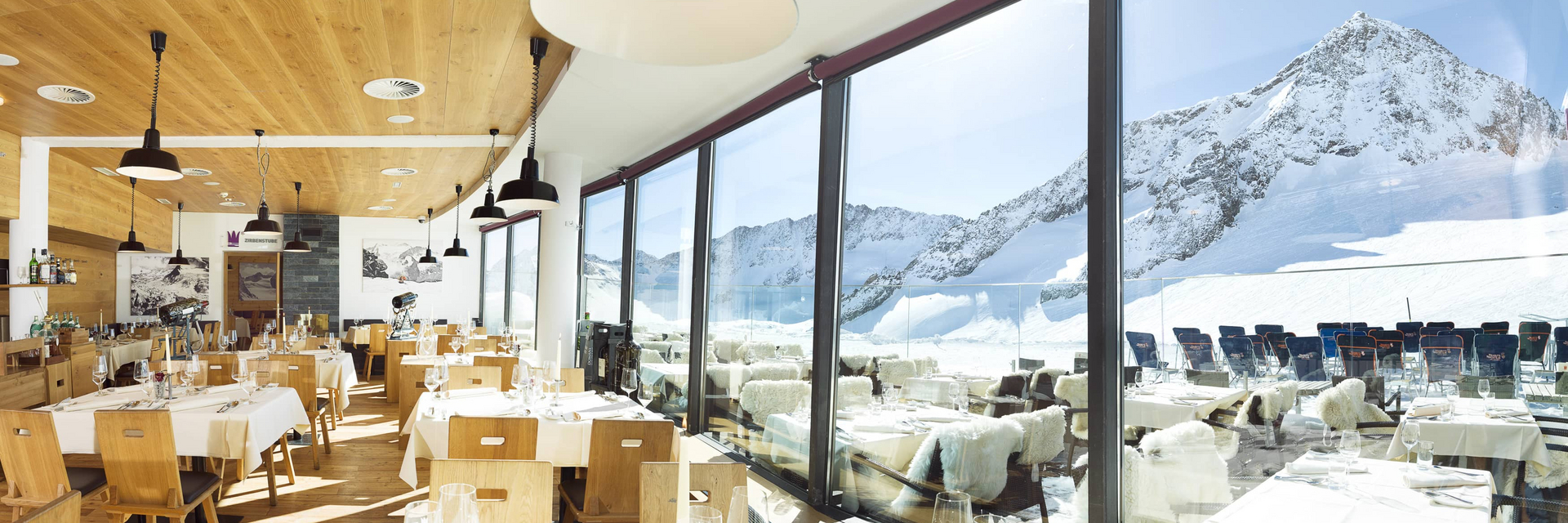 Set tables in the Schaufelspitz indoor area with view of the ski area in the winter